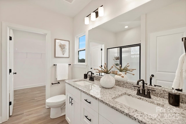 full bathroom featuring a walk in closet, a sink, a shower stall, and wood finished floors