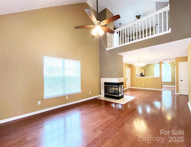 unfurnished living room with ceiling fan with notable chandelier, wood finished floors, a multi sided fireplace, and baseboards