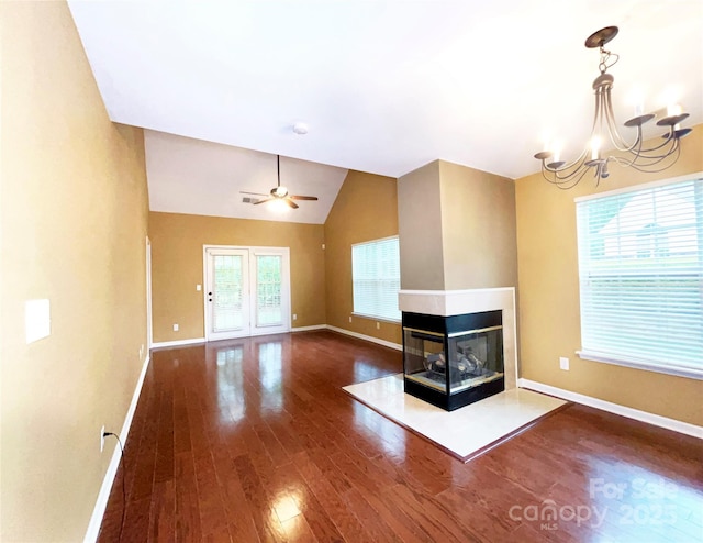 unfurnished living room featuring ceiling fan with notable chandelier, wood finished floors, a multi sided fireplace, baseboards, and vaulted ceiling