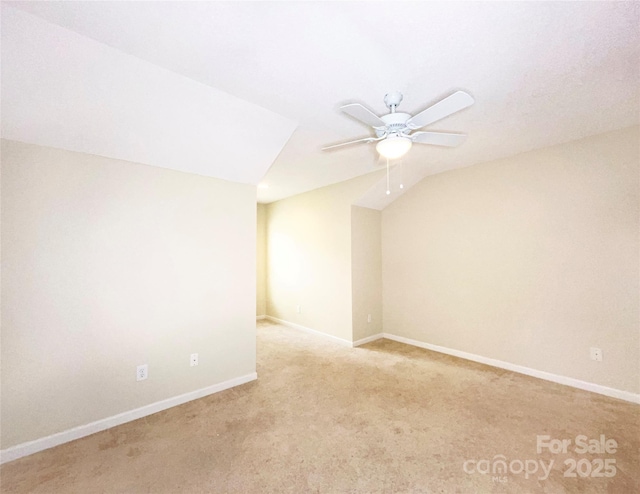 spare room featuring a ceiling fan, light colored carpet, vaulted ceiling, and baseboards