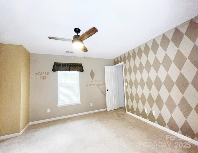 unfurnished room with an accent wall, visible vents, a ceiling fan, baseboards, and carpet