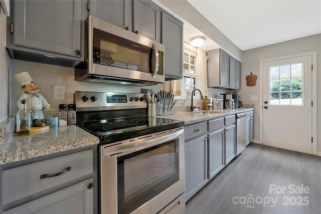 kitchen featuring gray cabinets, light stone counters, stainless steel appliances, and a sink