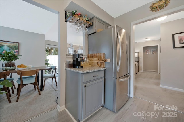 kitchen featuring light carpet, baseboards, gray cabinets, and freestanding refrigerator