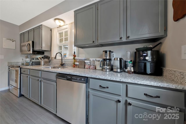 kitchen featuring appliances with stainless steel finishes, a sink, gray cabinetry, and light stone countertops