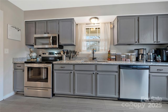 kitchen featuring stainless steel appliances, a sink, and gray cabinetry