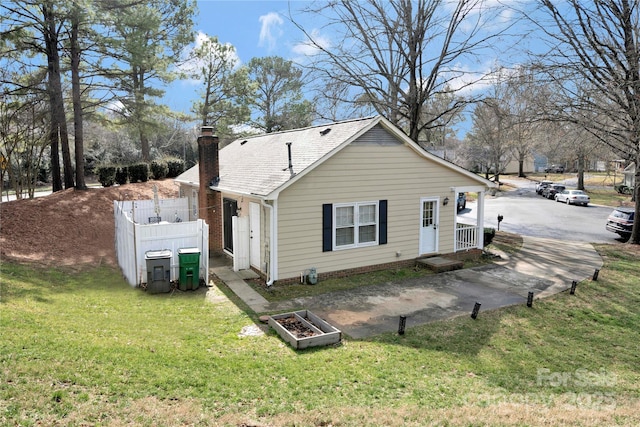 rear view of property with a shingled roof, fence, a chimney, and a lawn