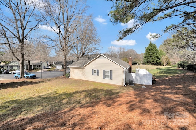 view of side of property featuring a yard, a chimney, a residential view, and central air condition unit