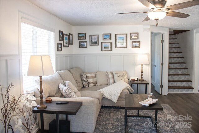 living room with a textured ceiling, a wainscoted wall, wood finished floors, a ceiling fan, and stairway