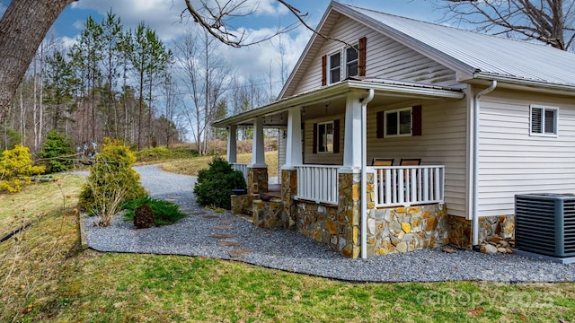 view of property exterior with covered porch, metal roof, stone siding, and cooling unit