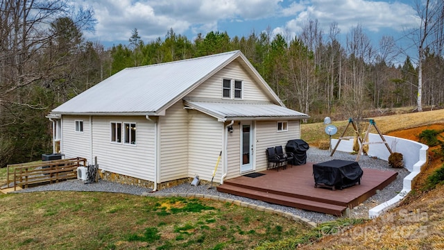 rear view of house with metal roof, a yard, a wooden deck, a forest view, and ac unit