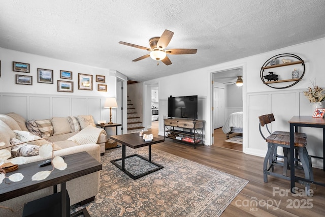 living room with a wainscoted wall, stairway, ceiling fan, a textured ceiling, and wood finished floors