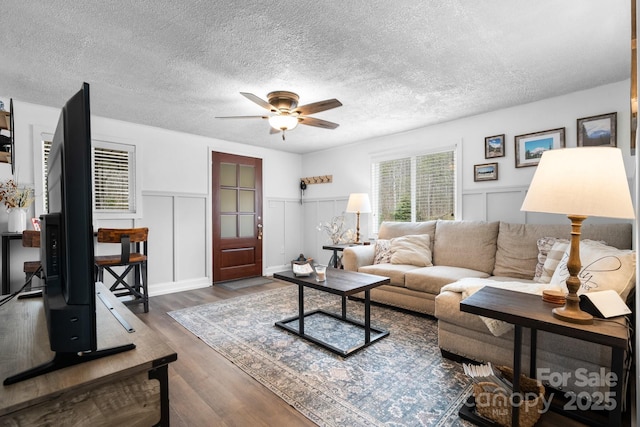 living room with a textured ceiling, wainscoting, wood finished floors, and a ceiling fan