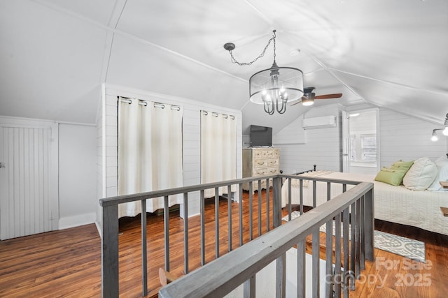 bedroom featuring vaulted ceiling, a wall mounted AC, wood finished floors, and a chandelier