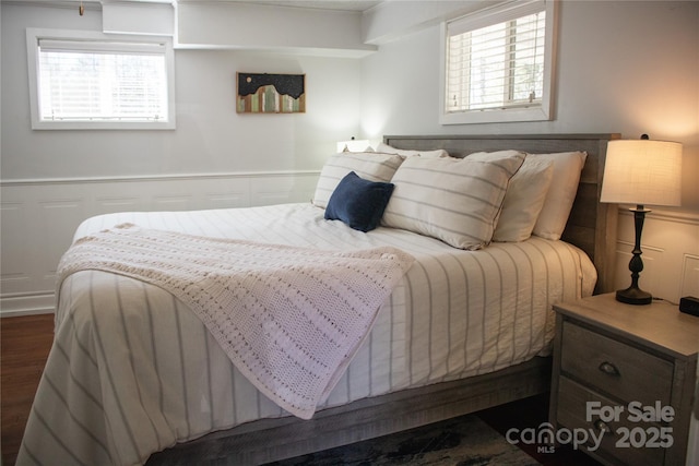 bedroom featuring dark wood-style floors, a wainscoted wall, a decorative wall, and multiple windows