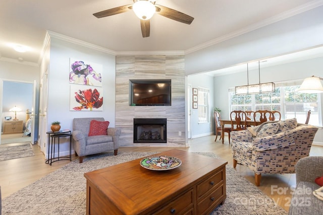 living room with light wood finished floors, baseboards, ceiling fan, ornamental molding, and a high end fireplace