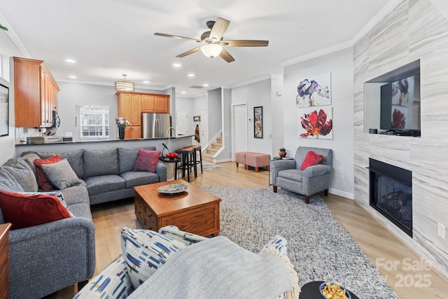 living room featuring a fireplace, crown molding, light wood finished floors, recessed lighting, and stairs