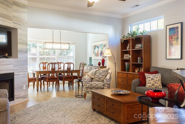 living area with visible vents, ornamental molding, a high end fireplace, a healthy amount of sunlight, and ceiling fan