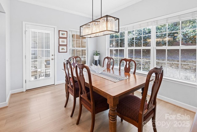 dining space featuring baseboards, a healthy amount of sunlight, ornamental molding, light wood-type flooring, and a notable chandelier