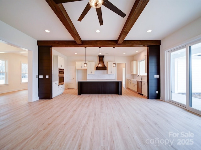 kitchen featuring open floor plan, hanging light fixtures, custom exhaust hood, light countertops, and white cabinetry