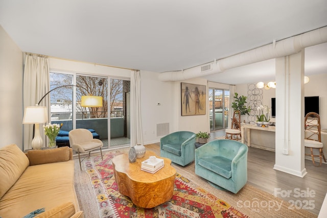 living room featuring an inviting chandelier, baseboards, visible vents, and wood finished floors