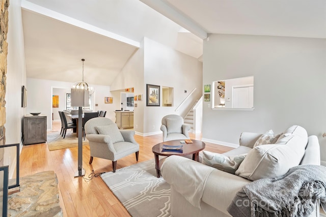 living area featuring a chandelier, light wood-style flooring, baseboards, stairs, and beam ceiling