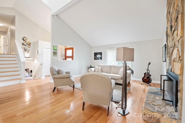 living area with high vaulted ceiling, a stone fireplace, light wood-style flooring, baseboards, and stairs