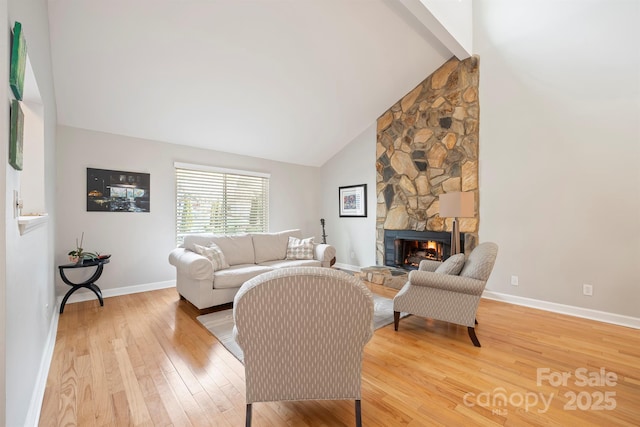 living area with high vaulted ceiling, baseboards, a stone fireplace, and light wood finished floors