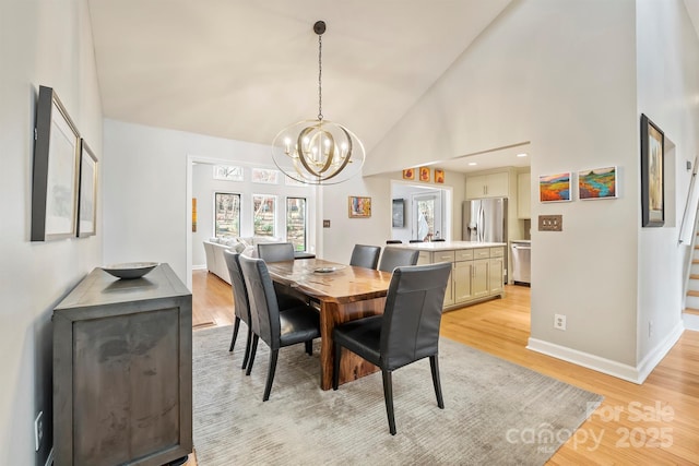 dining area with a chandelier, high vaulted ceiling, light wood-type flooring, and baseboards