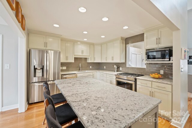 kitchen with appliances with stainless steel finishes, decorative backsplash, light stone counters, and a center island