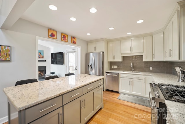 kitchen featuring a warm lit fireplace, a center island, stainless steel appliances, light wood-type flooring, and a sink