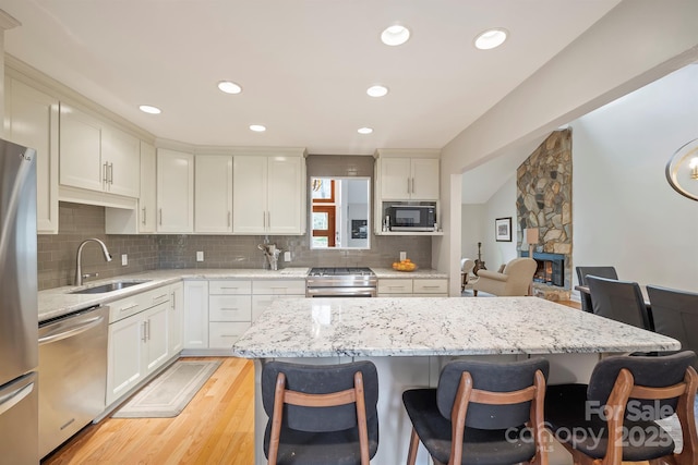 kitchen with light wood finished floors, a breakfast bar, stainless steel appliances, a stone fireplace, and a sink