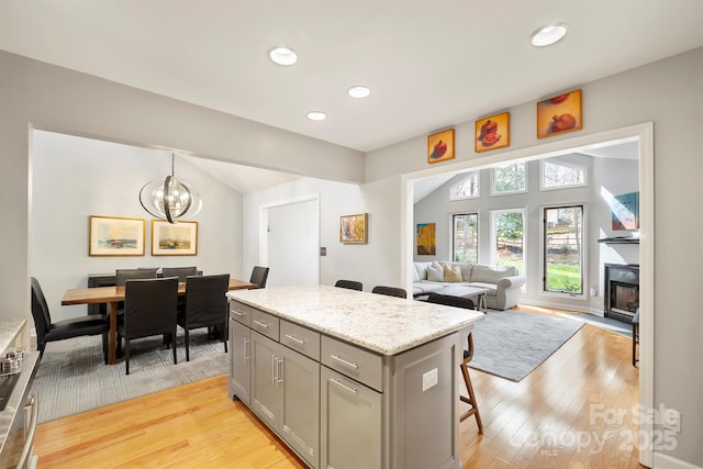 kitchen featuring vaulted ceiling, light wood finished floors, gray cabinets, and a kitchen breakfast bar