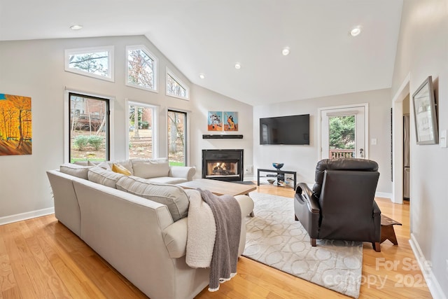 living room featuring recessed lighting, a glass covered fireplace, high vaulted ceiling, light wood-type flooring, and baseboards