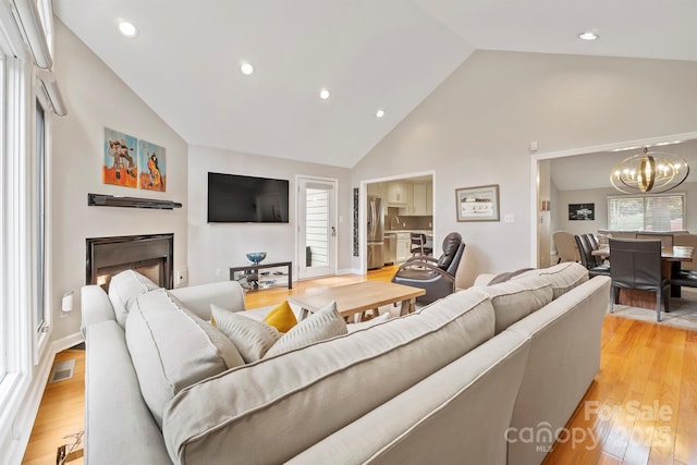 living room featuring light wood-style floors, plenty of natural light, visible vents, and an inviting chandelier