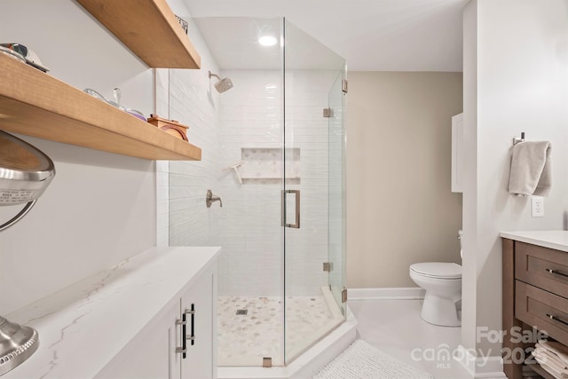 full bath featuring toilet, a stall shower, vanity, baseboards, and tile patterned floors