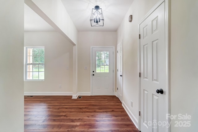 foyer entrance featuring dark wood-type flooring, a chandelier, and baseboards