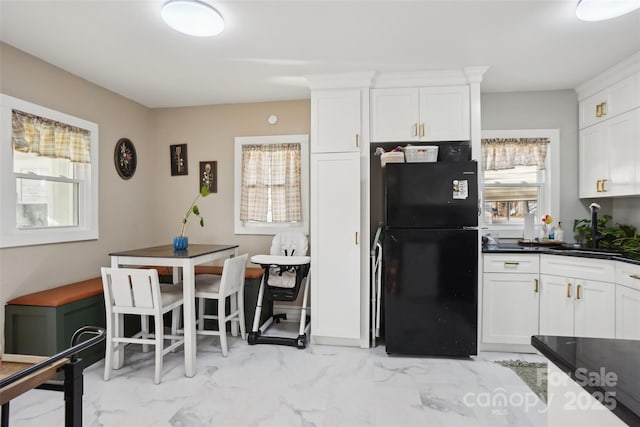 kitchen featuring marble finish floor, white cabinetry, a sink, and freestanding refrigerator