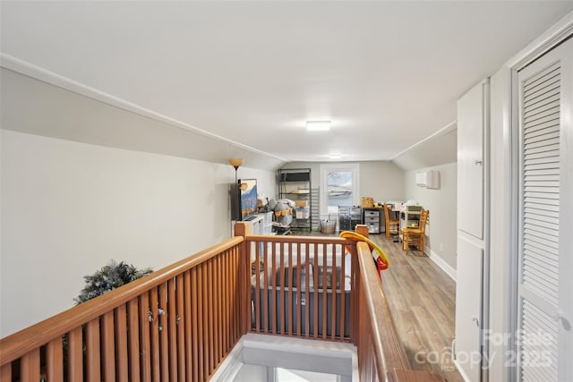 corridor with lofted ceiling, baseboards, wood finished floors, and an upstairs landing