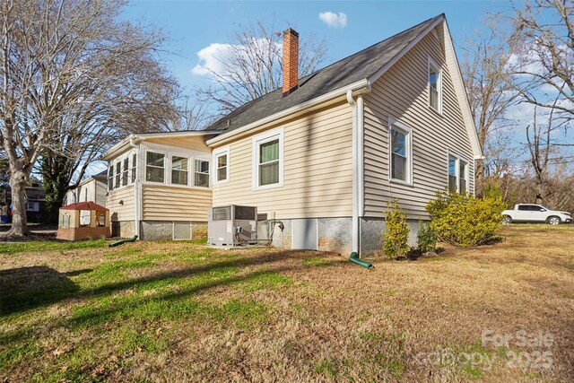 back of house with central air condition unit, a chimney, and a yard