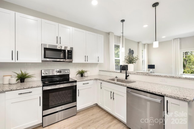 kitchen featuring light stone counters, a sink, white cabinets, appliances with stainless steel finishes, and decorative light fixtures