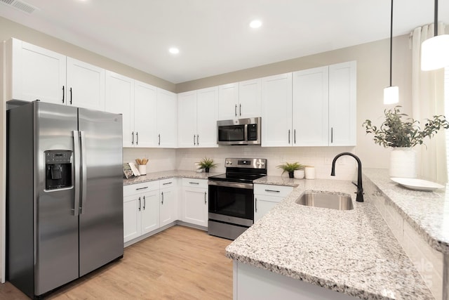 kitchen with light stone counters, stainless steel appliances, hanging light fixtures, white cabinets, and a sink