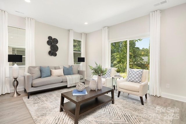 living room featuring baseboards, a wealth of natural light, visible vents, and light wood-style floors