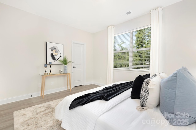 bedroom with wood finished floors, visible vents, and baseboards