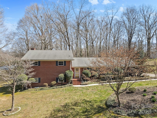 split level home with brick siding, a chimney, and a front lawn