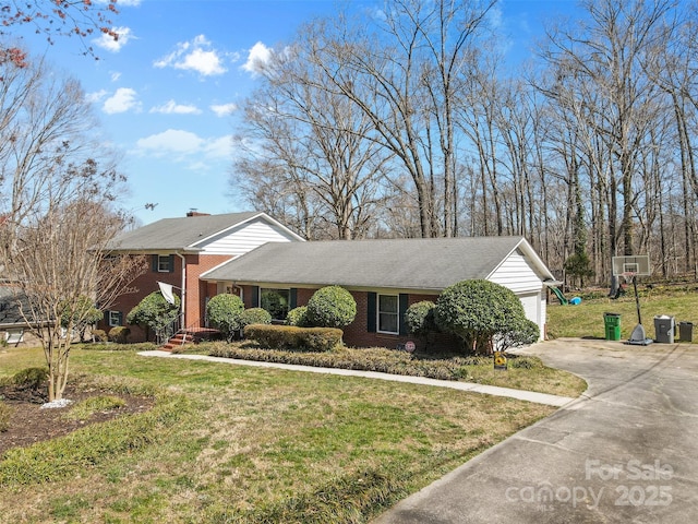 view of front facade featuring a front lawn, a garage, brick siding, and driveway