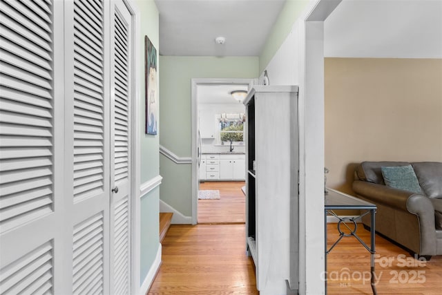 corridor with baseboards, light wood-style floors, and a sink