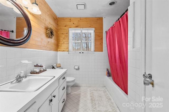 bathroom featuring tile patterned flooring, wood walls, shower / bath combo with shower curtain, toilet, and vanity