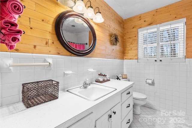 bathroom with vanity, a wainscoted wall, tile patterned flooring, tile walls, and toilet