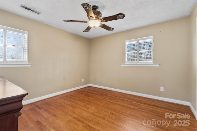 spare room with a wealth of natural light, visible vents, baseboards, and wood finished floors