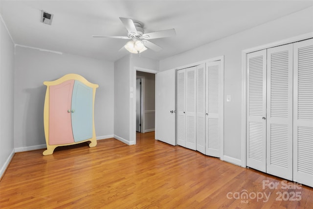 unfurnished bedroom with visible vents, baseboards, ceiling fan, light wood-style floors, and multiple closets